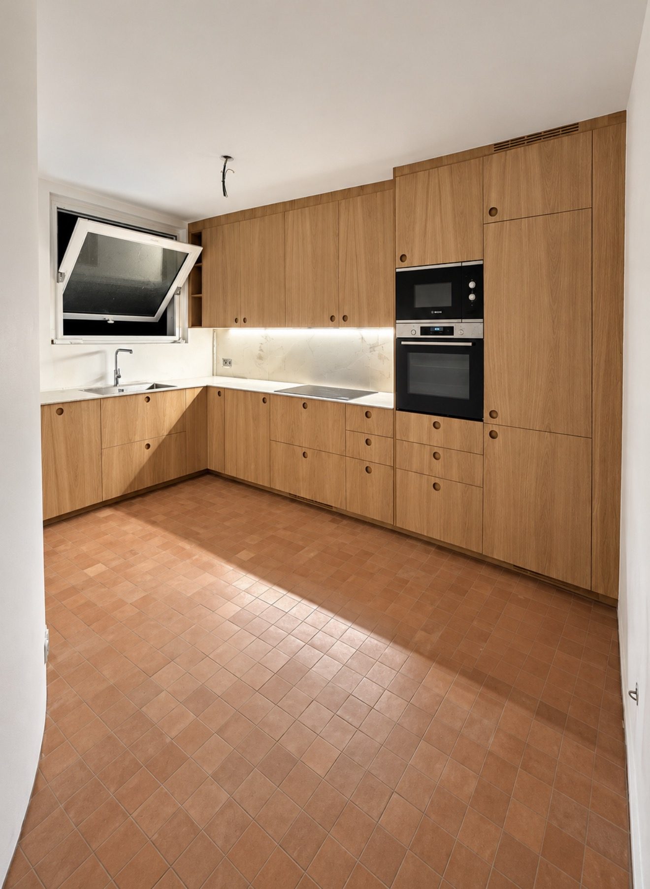 Cuisine en chêne à poignées rondes, plan et crédence blancs veinés, colonne four et micro-ondes encastrés, sol en tomettes — chantier réel en Île-de-France